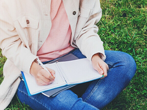 草むらに座ってノートに何かを書いているイメージ画像